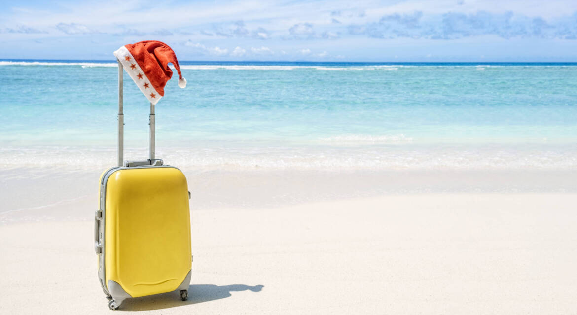 yellow-hardshell-carry-on-roller-luggage-with-red-santa-hat-on-a-sandy-beach-scaled.jpg